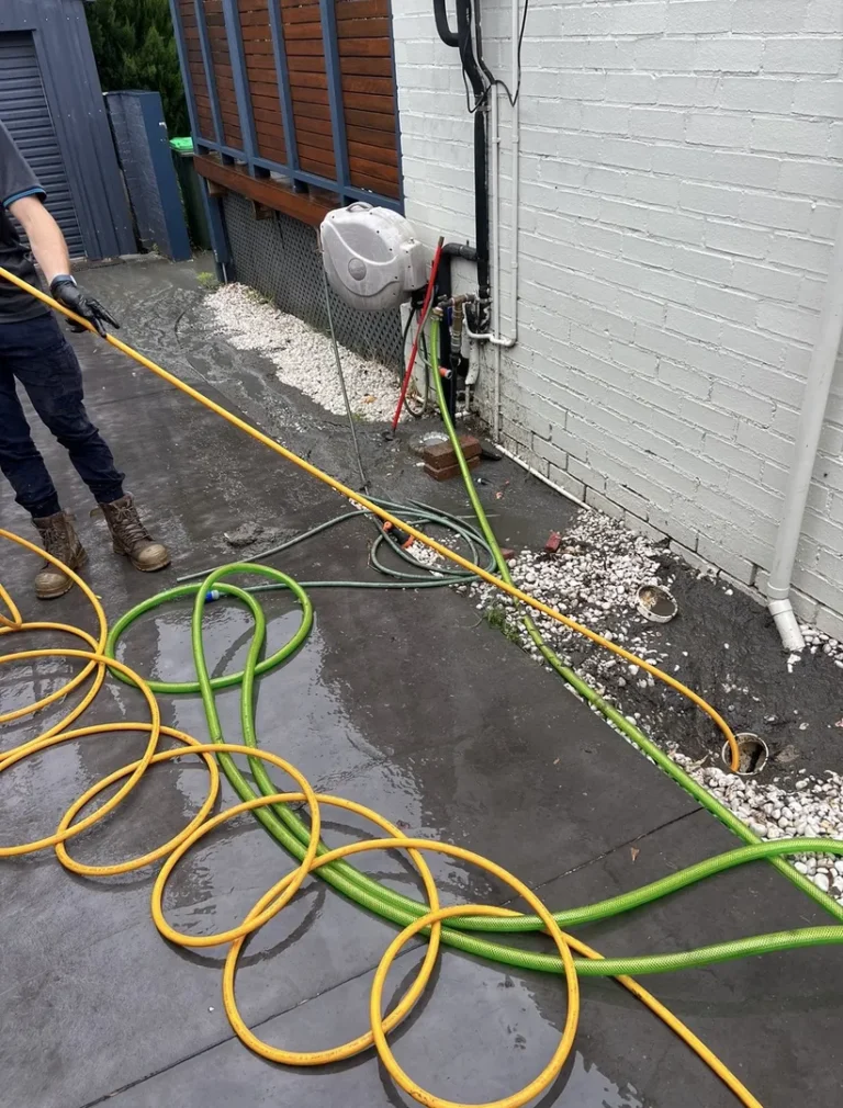 Worker handling tangled water hoses outside building.